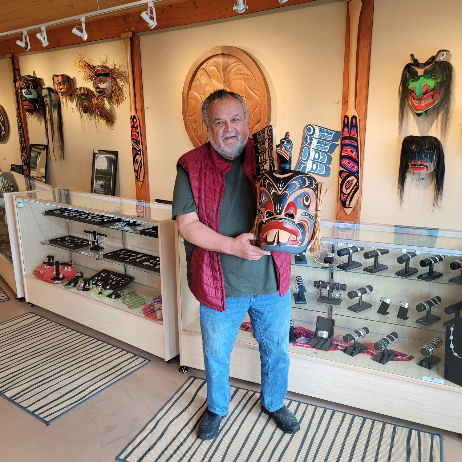 Kwakwaka'wakw artist Bill Henderson holding hand-carved Pugwis and Raven Indigenous Mask